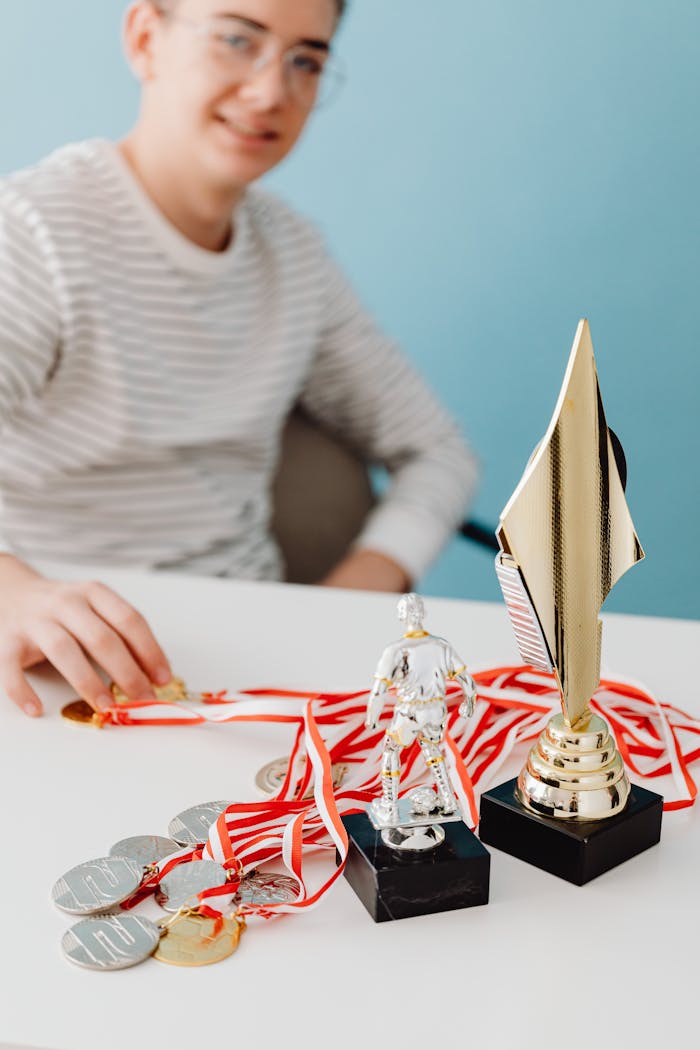 Person with trophies and medals on a white table, symbolizing success and achievement.