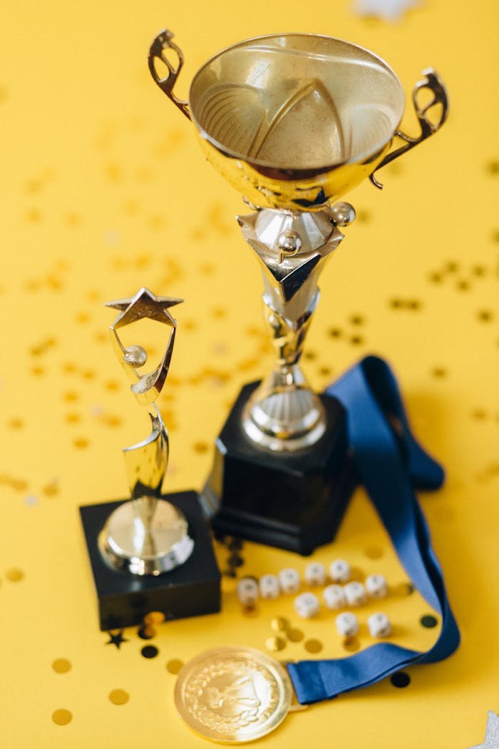 Golden trophies and medal displayed on a confetti-strewn yellow background.