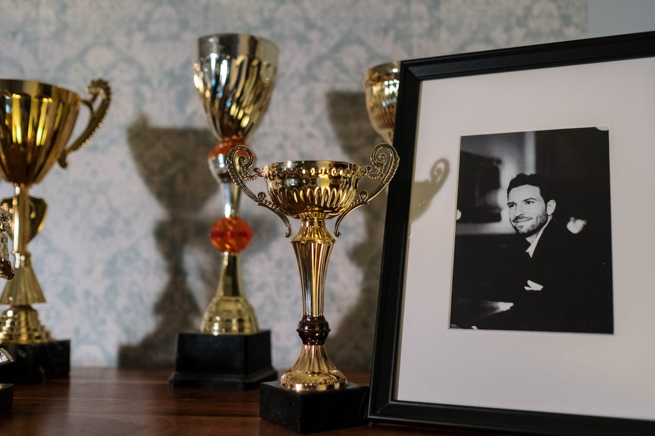 about-us A collection of trophies with a framed black and white portrait on a shelf.